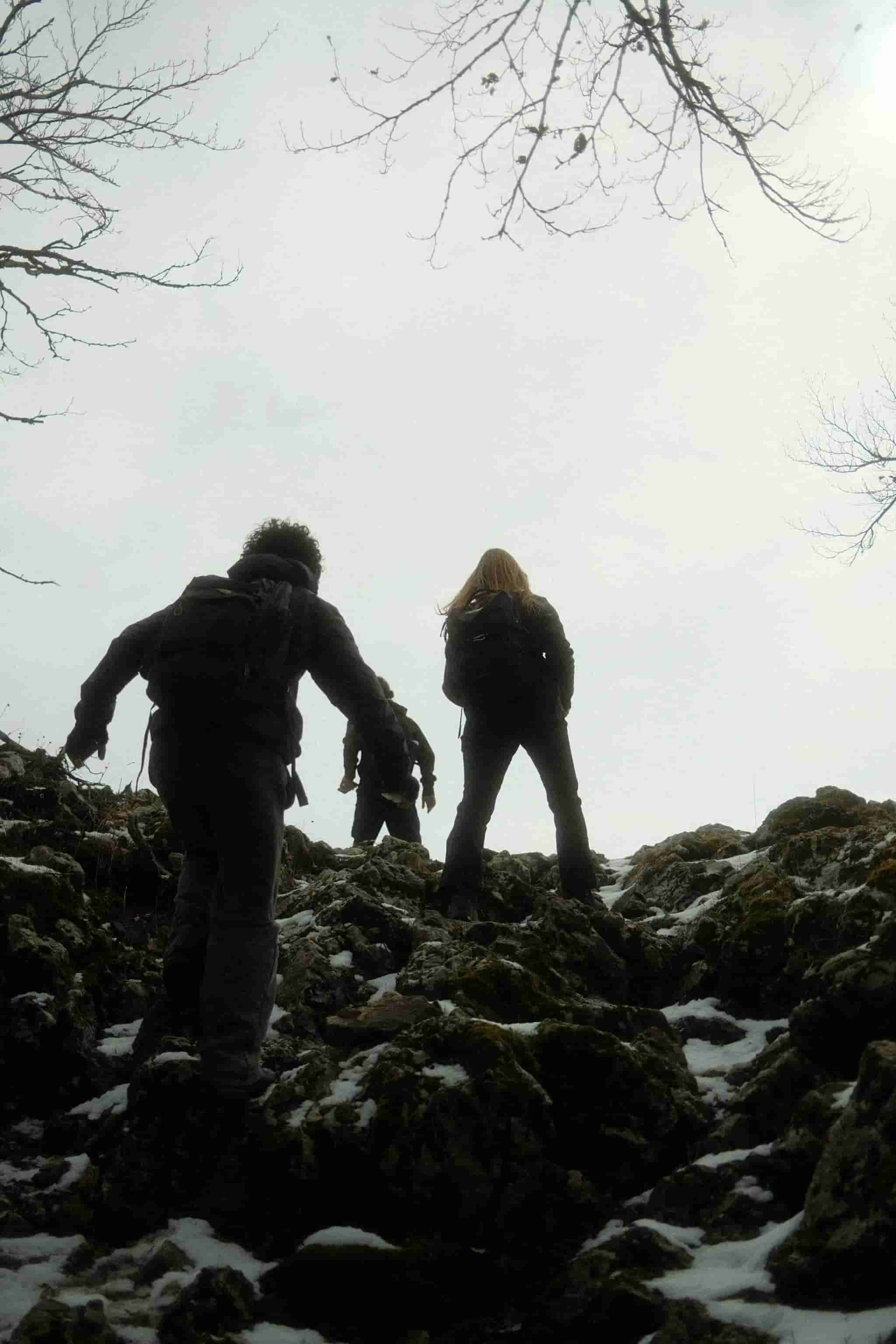 Sagome controluce che salgono su rocce innevate